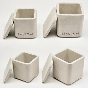 May include: Four square concrete containers with lids. The containers are in different sizes. The containers are labelled with their volume in ounces and millilitres. 7 oz / 200 ml, 12.5 oz / 370 ml.