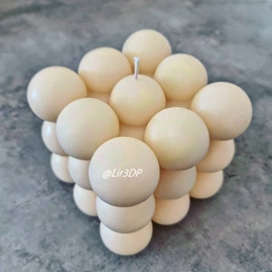 May include: A white candle shaped like a cube with a single wick. The cube is made up of many small spheres.