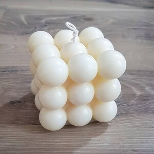 Könnte beinhalten: Eine weiße, würfelförmige Kerze mit einer strukturierten Oberfläche. Die Kerze besteht aus vielen kleinen Kugeln.