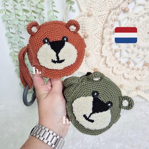 May include: Two crocheted bear-shaped toys with smiling faces. One is brown with a gray loop and the other is green. Both have black eyes and noses.