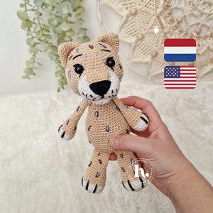 Op de afbeelding: Een gehaakt cheetah-speeltje in beige met zwarte en paarse vlekken. De cheetah heeft een witte snuit, zwarte ogen en een zwarte neus. Het speelgoed heeft een vriendelijke uitdrukking.