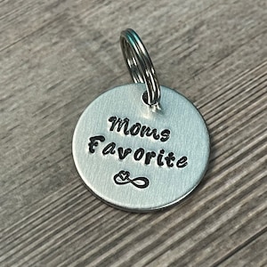 May include: Silver keychain with a round tag that says "Mom's Favorite" with an infinity symbol and a heart.