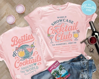 Könnte beinhalten: Zwei rosa T-Shirts mit Cocktail-Designs. Eines zeigt "World Showcase Cocktail Club", das andere "Besties & Cocktails Around The World". Das Bild enthält Jeans, Wein, einen Korkenzieher und Cocktailgläser.