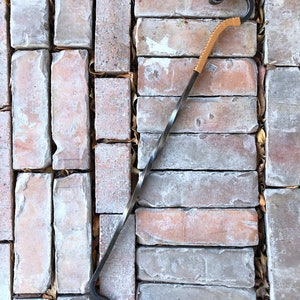 May include: A long, twisted metal fireplace poker with a leather handle. The poker has a hook on each end and is designed to move logs in a fireplace.