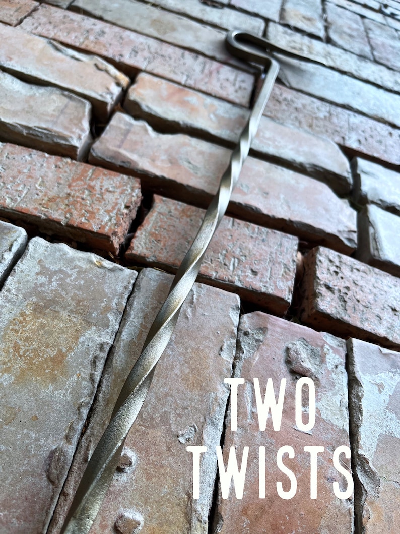 May include: A twisted metal fireplace poker with a hook on the end. The poker is resting against a brick wall. The text "TWO TWISTS" is visible in the image.