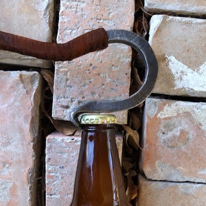 May include: A brown leather-wrapped bottle opener with a metal hook, opening a brown glass bottle.