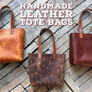 May include: Three handmade leather tote bags in different shades of brown. The bags have a simple design with a single strap and a top zipper closure.  HANDMADE LEATHER TOTE BAGS is written in white text on a brick background.