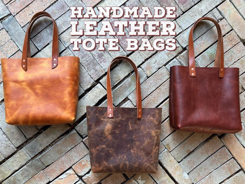 May include: Three handmade leather tote bags in different shades of brown. The bags have a simple design with a single strap and a top zipper closure.  HANDMADE LEATHER TOTE BAGS is written in white text on a brick background.