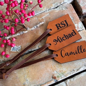May include: Three brown leather gift tags with black lettering. The tags are tied with brown leather cords. The tags are labeled "RSJ", "Michael", and "Camille".