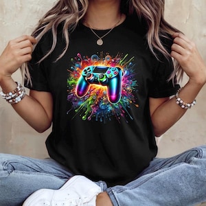 May include: Black t-shirt featuring a vibrant, colorful graphic of a video game controller. The controller is rendered in shades of blue, teal, and pink, with a splash of rainbow colors emanating from behind it. The design is eye-catching and bold.