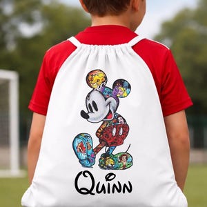 May include: White drawstring backpack featuring a colorful Mickey Mouse design with various Disney characters. The name "Quinn" is printed in black script below the character. The backpack is worn by a person wearing a red and white baseball style shirt.