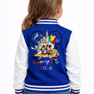 May include: A white ceramic mug with a black handle and the text "But First, Coffee" in a bold, black font. The mug is set against a blurred background. The mug appears to be approximately 10 cm tall.