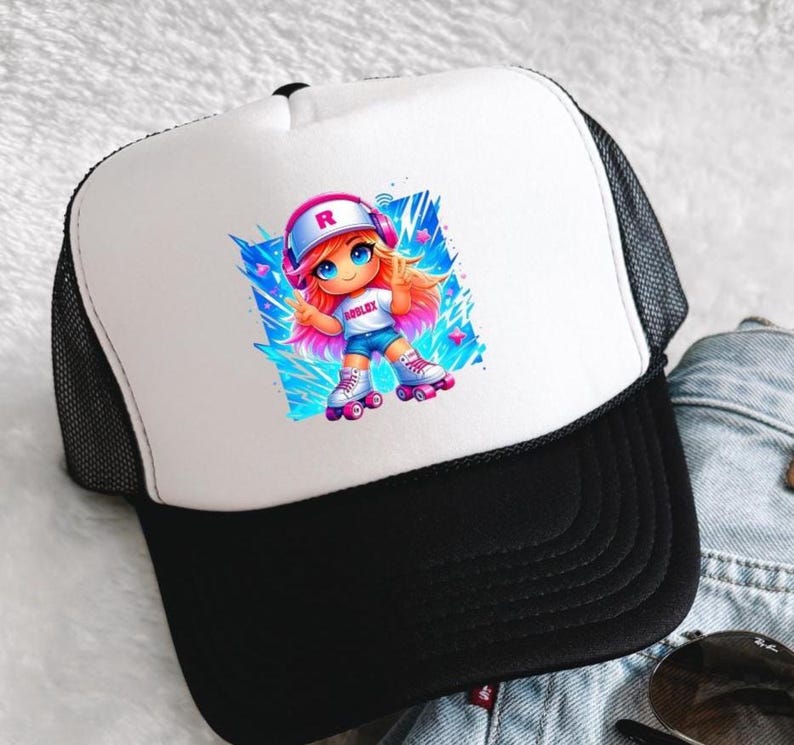 Op de afbeelding: Zwarte en witte truckerpet met een wit voorpaneel. Het paneel toont een cartoonmeisje op rolschaatsen. Het meisje heeft oranje haar en draagt een shirt met het woord "ROBLOX". De pet heeft een zwarte klep en een mesh achterkant.