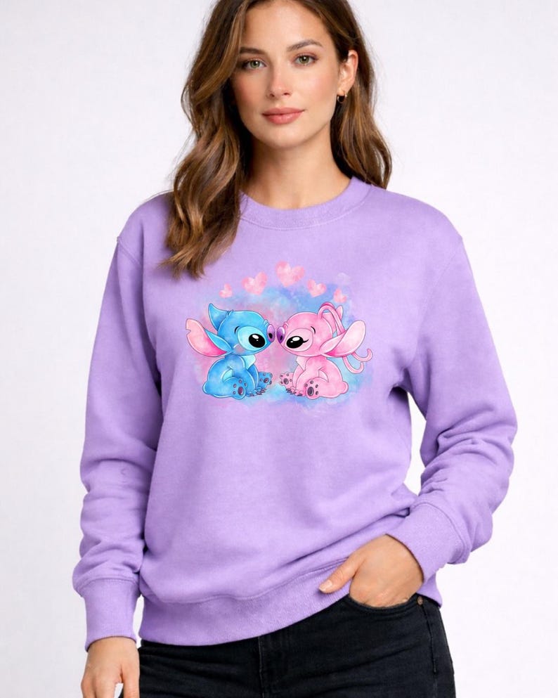 Puede incluir: Una sudadera lavanda con un dise&ntilde;o de los personajes Stitch y Angel de la pel&iacute;cula de Disney Lilo & Stitch. Stitch azul y Angel rosa se representan abrazados, rodeados de corazones rosas.