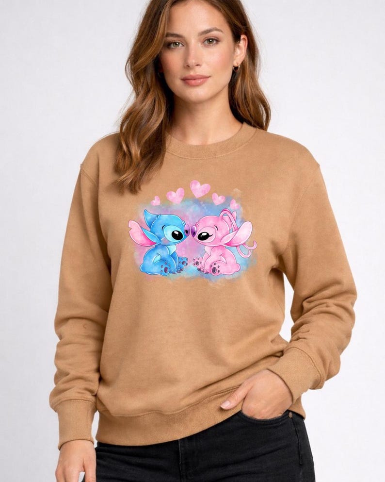 Puede incluir: Una sudadera marr&oacute;n con un gr&aacute;fico de dos personajes de dibujos animados, uno azul y otro rosa, con corazones encima. Los personajes est&aacute;n sobre un fondo de acuarela azul y rosa. La sudadera tiene mangas largas.