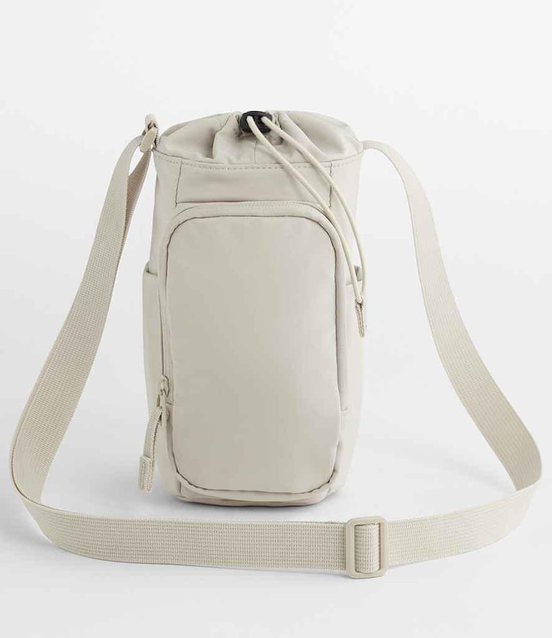 May include: A beige crossbody bag with a drawstring closure at the top. The bag has a front pocket with a zipper and an adjustable shoulder strap. The bag is made of a smooth, durable material.