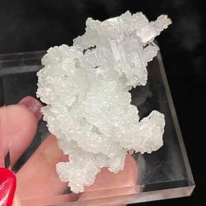May include: A cluster of white, translucent, crystalline formations. The crystals are small and densely packed, creating a textured, almost fluffy appearance.