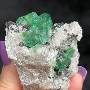K&ouml;nnte beinhalten: Ein Cluster gr&uuml;ner Fluoritkristalle auf einer Matrix aus wei&szlig;em Calcit und grauem Bleiglanz. Die Fluoritkristalle sind scharf und gut ausgebildet, mit einem glasartigen Glanz.