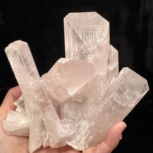 以下が含まれることがあります： 淡いピンク色の結晶の塊。結晶構造があり、内部に縞模様が見える半透明の品質です。全体的な形状は不規則で、複数のポイントとファセットがあります。背景は黒です。