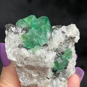 K&ouml;nnte beinhalten: Ein Cluster gr&uuml;ner Fluoritkristalle auf einer wei&szlig;en Matrix. Die Kristalle sind scharf und gut ausgebildet, mit einem glasartigen Glanz. Die Matrix ist mit kleinen, wei&szlig;en Kristallen bedeckt.