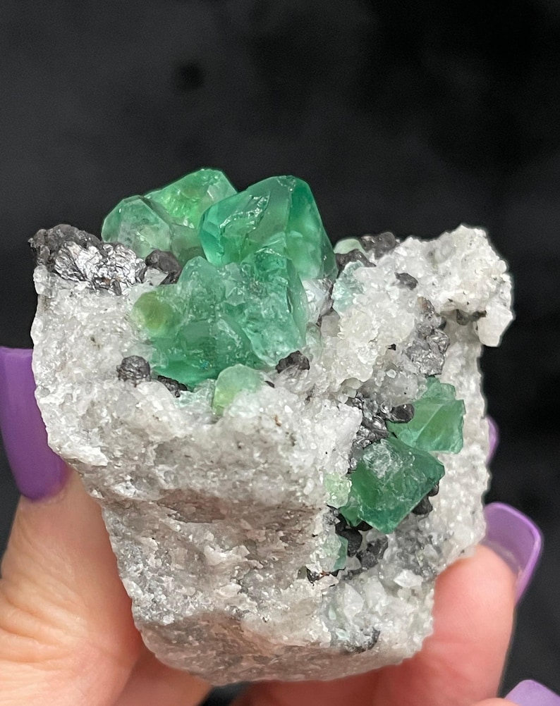 K&ouml;nnte beinhalten: Ein Cluster gr&uuml;ner Fluoritkristalle auf einer wei&szlig;en Matrix. Die Kristalle sind scharf und gut ausgebildet, mit einem glasartigen Glanz. Die Matrix ist mit kleinen, wei&szlig;en Kristallen bedeckt.
