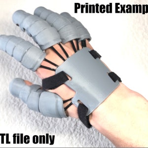 May include: A 3D printed gray hand with articulated fingers and a wrist strap. The hand is designed to be worn on the left hand. The image includes the text "Printed Example" and ".STL file only".