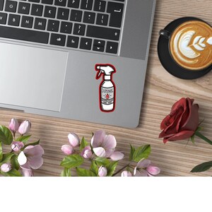 May include: A white sticker with a red border featuring a cartoon illustration of a spray bottle labeled "Luminol" with a red drop of liquid. The bottle is on a silver laptop.