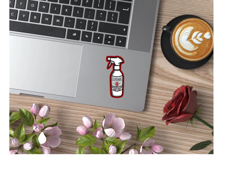 May include: A white sticker with a red border featuring a cartoon illustration of a spray bottle labeled "Luminol" with a red drop of liquid. The bottle is on a silver laptop.