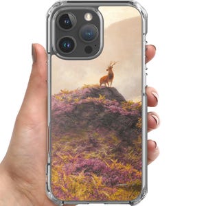 Może przedstawiać: Przezroczyste etui na telefon z obrazem jelenia na wzgórzu pokrytym fioletowymi i żółtymi kwiatami. Tło przedstawia pasmo górskie pod zachmurzonym niebem. Etui ma przezroczysty zderzak.