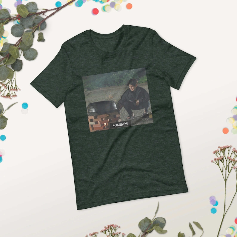 May include: A dark green t-shirt with a graphic of a person crouching next to a pot with the text "HAJIMA!" printed below the image.