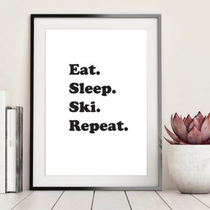 Op de afbeelding: Zwart-wit ingelijste print met de tekst "Eat. Sleep. Ski. Repeat."