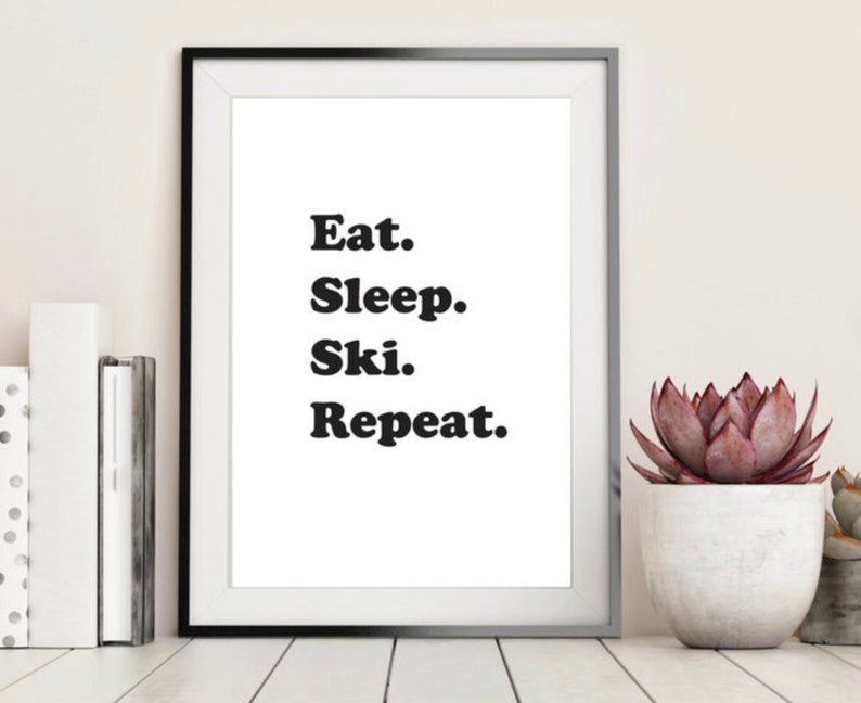 Op de afbeelding: Zwart-wit ingelijste print met de tekst "Eat. Sleep. Ski. Repeat."