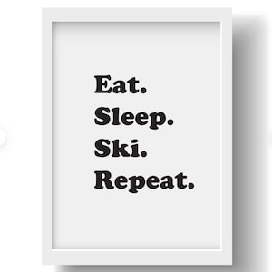 Op de afbeelding: Een wit ingelijst print met zwarte tekst die "Eten. Slapen. Ski&euml;n. Herhalen." luidt.
