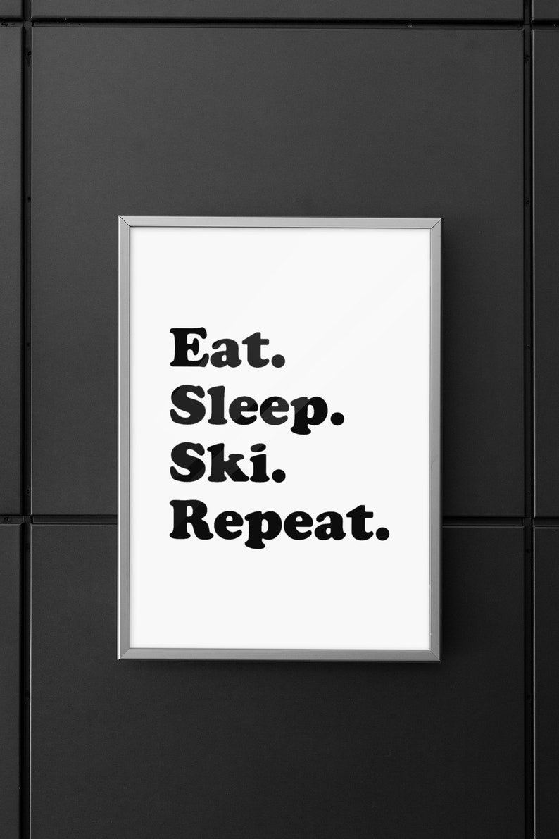 Op de afbeelding: Een ingelijst print met de tekst "Eat. Sleep. Ski. Repeat." in zwarte vetgedrukte letters op een witte achtergrond.