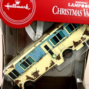 May include: A Hallmark Christmas Vacation ornament featuring a rusty, yellow, and blue camper van with the text "National Lampoon's Christmas Vacation" on the packaging.