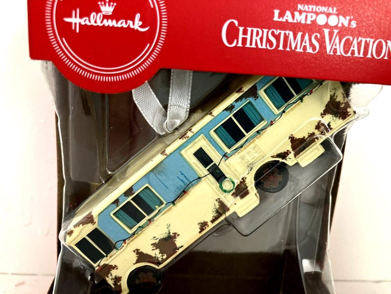May include: A Hallmark Christmas Vacation ornament featuring a rusty, yellow, and blue camper van with the text "National Lampoon's Christmas Vacation" on the packaging.