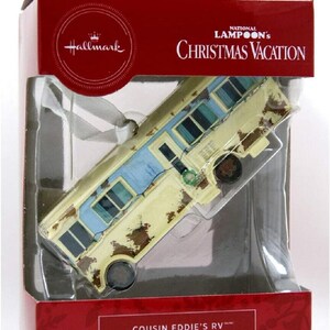 May include: A Hallmark Christmas Vacation ornament featuring Cousin Eddie's RV. The ornament is a detailed replica of the iconic RV from the movie, with a yellow and blue paint scheme and rust detailing. The ornament is packaged in a red box with the National Lampoon's Christmas Vacation logo.