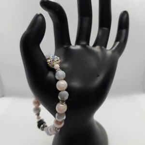 May include: A bracelet made of pink, gray, and clear beads with a sparkly silver and clear bead in the center.