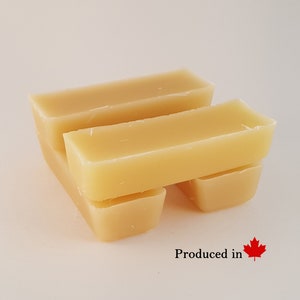 May include: Three rectangular blocks of yellow beeswax stacked on top of each other. The blocks are smooth and have a slight sheen. The text "Produced in" and a Canadian flag are visible below the blocks.