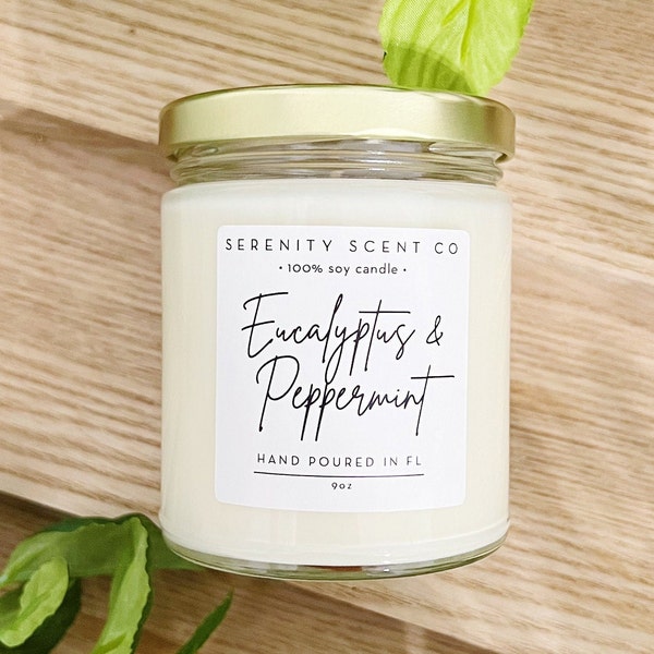 Può includere: Candela in barattolo di vetro con coperchio dorato. L'etichetta recita "Eucalyptus & Peppermint" e "Hand Poured in FL". La candela è da 255g ed è realizzata con cera di soia al 100%. Lo sfondo è una superficie di legno chiaro.