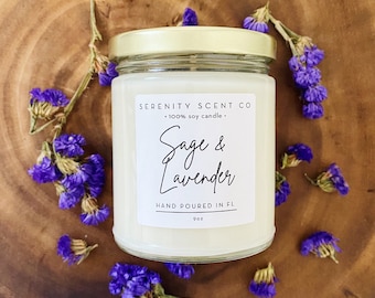 Può includere: Una candela in barattolo di vetro con coperchio dorato, etichettata "Sage & Lavender" e "100% soy candle." La candela è circondata da piccoli fiori viola su una superficie di legno. L'etichetta dice anche "HAND POURED IN FL" e "9oz."