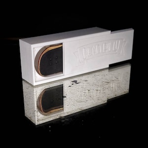 May include: White box with a sliding lid, revealing a small wooden fingerboard with black grip tape. The box has the text "Dead Bull" printed on it.