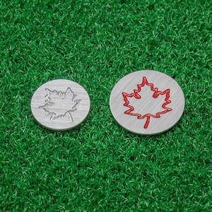 Peut inclure: Deux marqueurs de balle de golf argentés avec un motif de feuille d'érable. Un marqueur a une feuille d'érable rouge et l'autre a une feuille d'érable argentée.