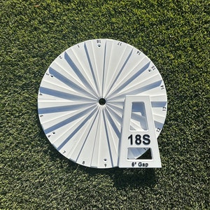 May include: White golf club yardage marker with a 6-degree gap and a white plastic stand. The marker has numbers 1 through 18 around the edge.