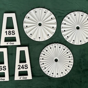 Puede incluir: Tres guías circulares de plástico blanco con números negros y un punto negro en el centro. Las guías están etiquetadas como 18S, 24S y 36S. Cada guía tiene un número diferente de secciones. Las guías están sobre una superficie verde.