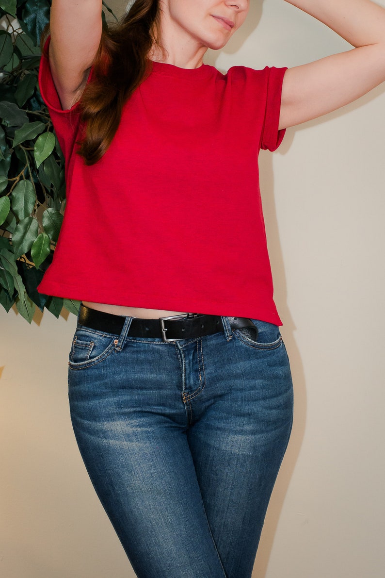 K&ouml;nnte beinhalten: Eine Frau tr&auml;gt ein rotes T-Shirt mit kurzen &Auml;rmeln und eine blaue Jeans mit einem schwarzen G&uuml;rtel.