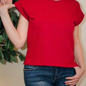 K&ouml;nnte beinhalten: Eine Frau tr&auml;gt ein rotes T-Shirt mit kurzen &Auml;rmeln und eine blaue Jeans.