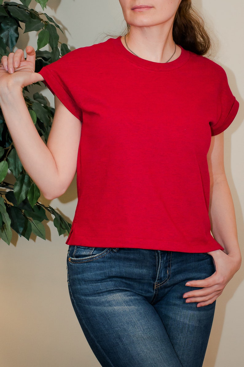 K&ouml;nnte beinhalten: Eine Frau tr&auml;gt ein rotes T-Shirt mit kurzen &Auml;rmeln und eine blaue Jeans.