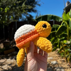 May include: A crocheted turtle toy with a white, orange, and yellow shell. The turtle has a yellow body and black eyes.