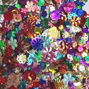 May include: A vibrant assortment of colorful sequins and embellishments. The image showcases a variety of shapes, including flowers, stars, and geometric designs, in shades of red, pink, gold, green, and purple. These decorative elements are ideal for crafting and embellishing projects.